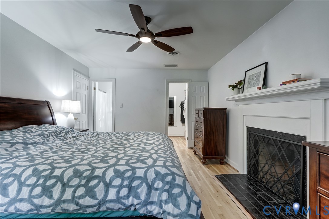 Fireplace with a white mantel and black tile hearth, wood-finish flooring, and a ceiling-mounted light fixture with fan blades