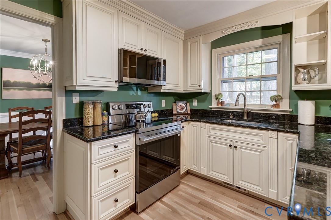 Kitchen featuring off-white cabinetry, dark stone countertops, stainless steel appliances, and a single-basin undermount sink