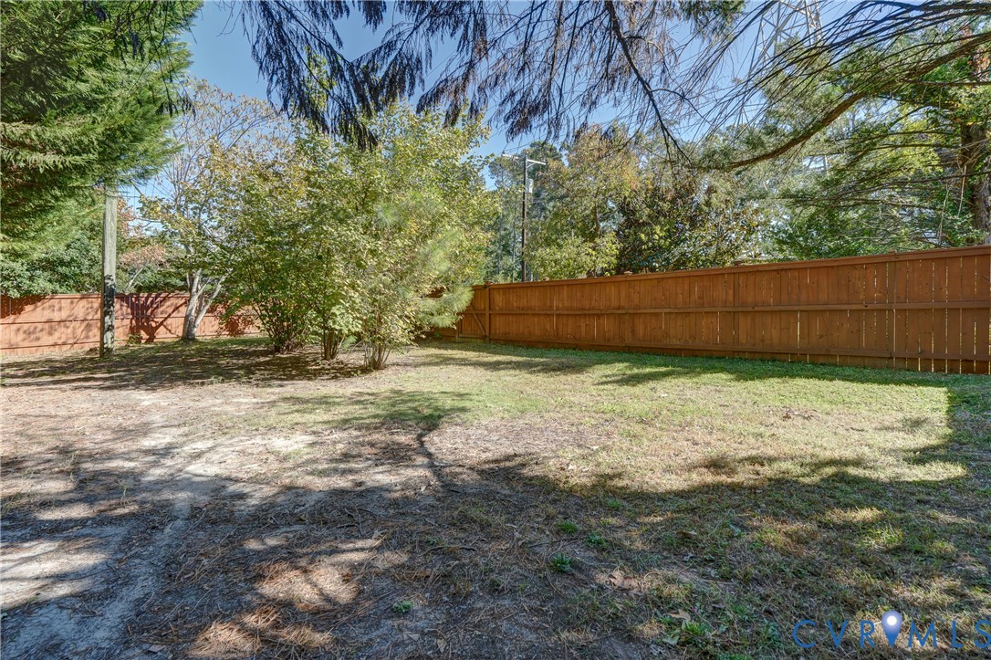 Backyard featuring a wood-panel fence, mature trees, and open lawn area