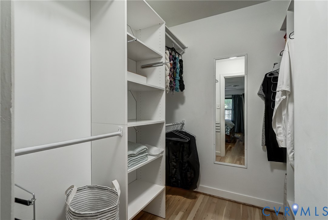 Walk-in closet featuring white built-in shelving, vertical storage compartments, dual-level hanging rods, and a wall-mounted mirror over wood-finish flooring