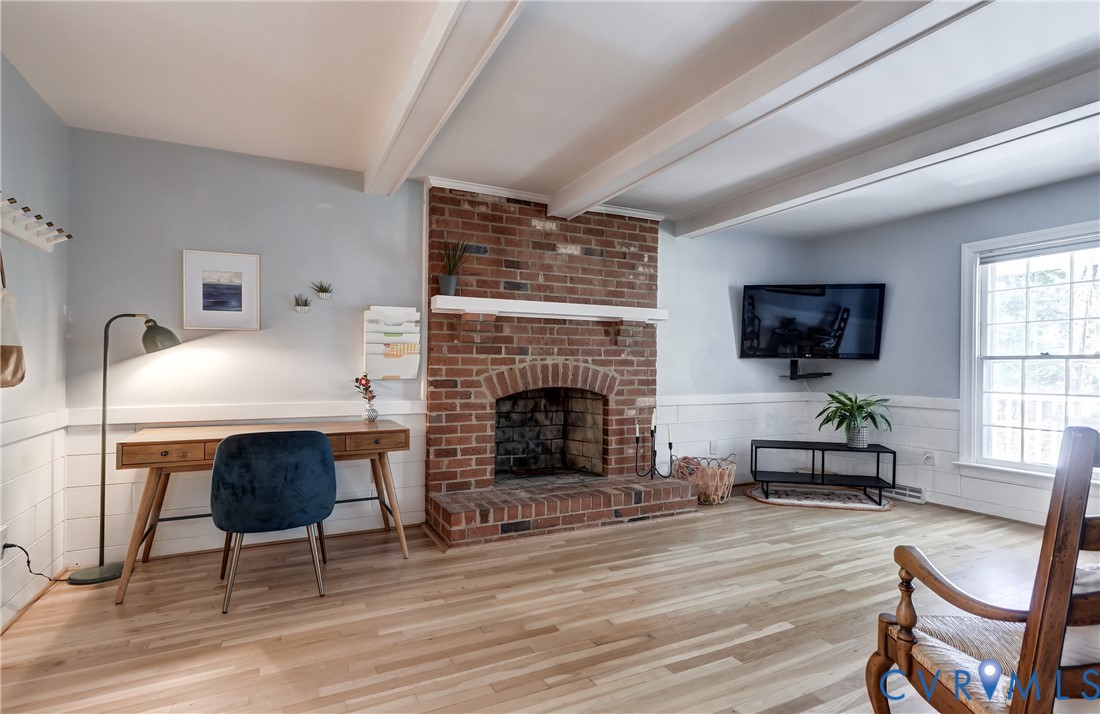 Exposed wood ceiling beams, red brick fireplace with a mantel, horizontal wood wall paneling, and light-toned wood-finish flooring