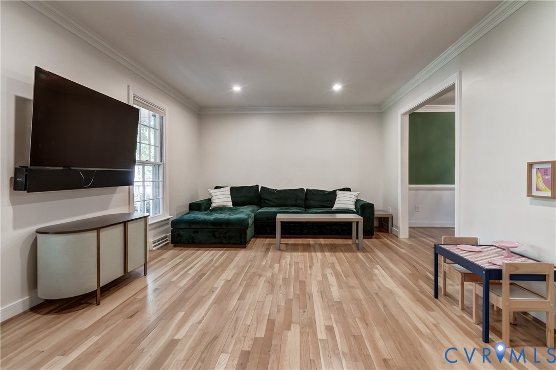 Living area featuring light wood-finish flooring, recessed lighting, crown molding, and a multi-pane window