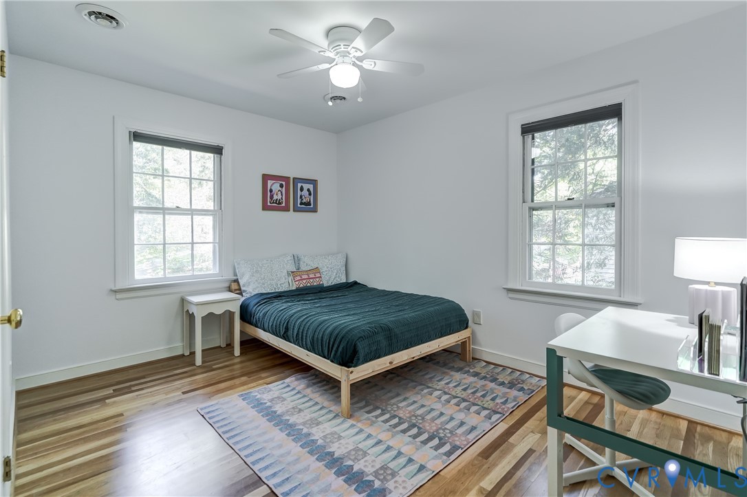 Room featuring wood-finish flooring, two double-hung windows with muntins, and a ceiling-mounted light fixture with a fan