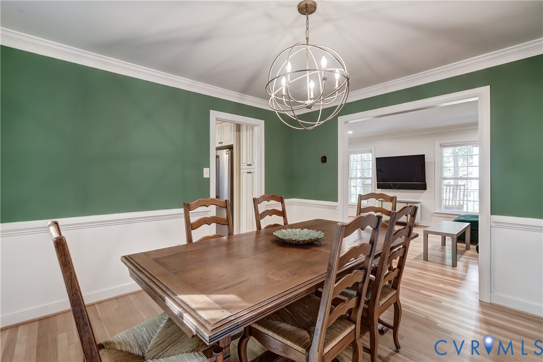 Dining area featuring wood-finish flooring, white crown molding, crisp chair rail trim, and a spherical metal chandelier