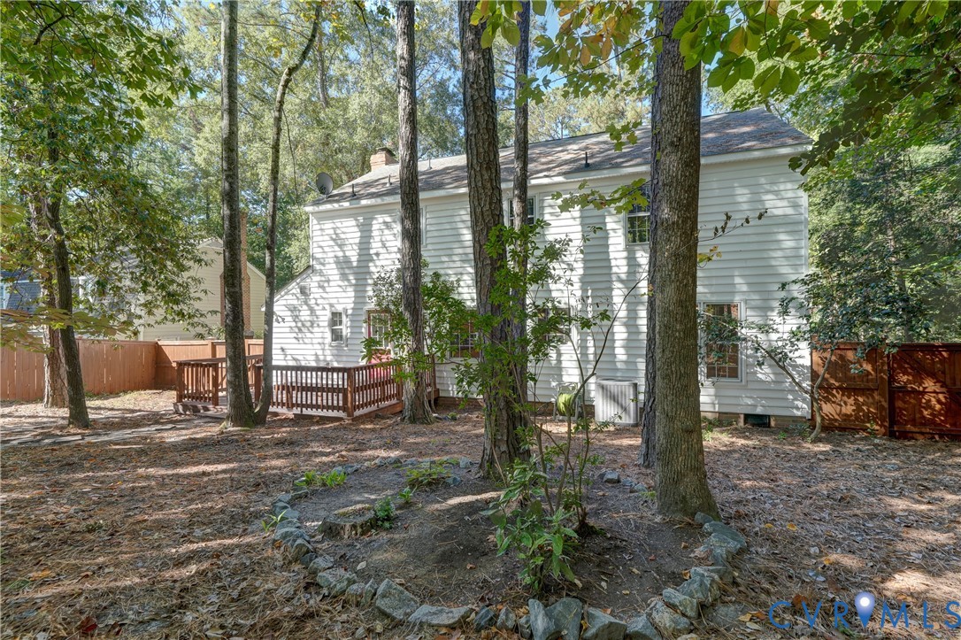 Two-story residence with white siding, rear wooden deck, stone-bordered landscaping, and wood privacy fencing
