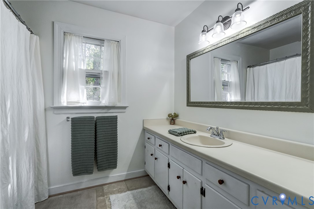 Bathroom featuring a wide white vanity with an integrated basin, a large framed wall-mounted mirror, a three-light fixture, and a window with molded trim