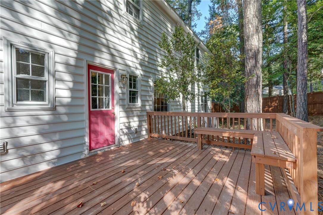 Wood-plank deck featuring a wrap-around built-in bench, light-colored horizontal lap siding, and a multi-pane glass-panel entry door