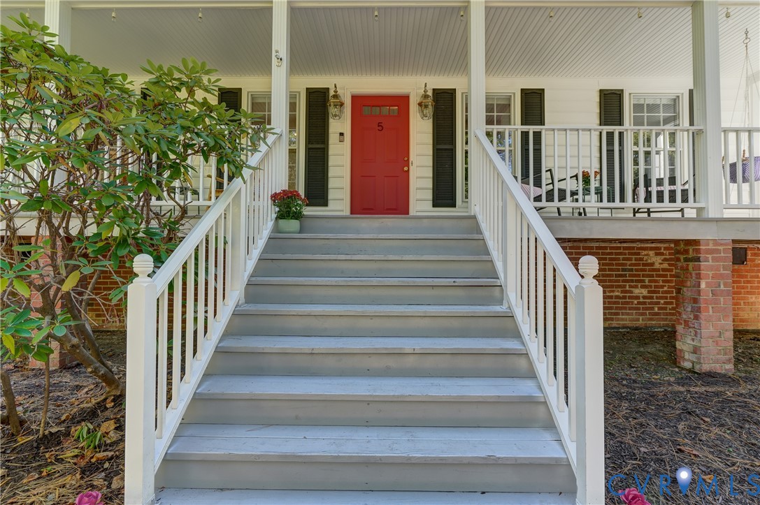 Covered front porch featuring white railing, brick foundation detailing, wide staircase, and a central paneled door Covered front porch featuring white railing, brick foundation detailing, wide staircase, and a central paneled door
