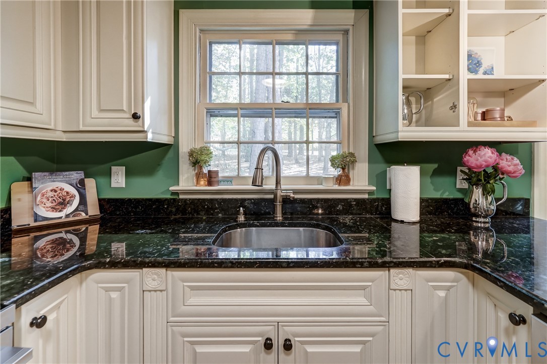 Kitchen featuring custom cabinetry with decorative molding, dark stone countertops, an undermount stainless steel sink, a high-arc pull-down faucet, and open display shelving