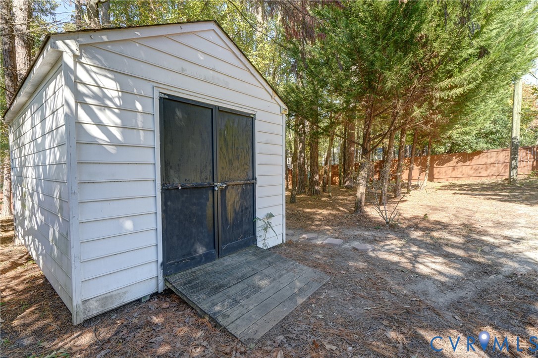 Exterior storage structure featuring white horizontal siding, double entry doors, a wooden ramp, and mature perimeter trees