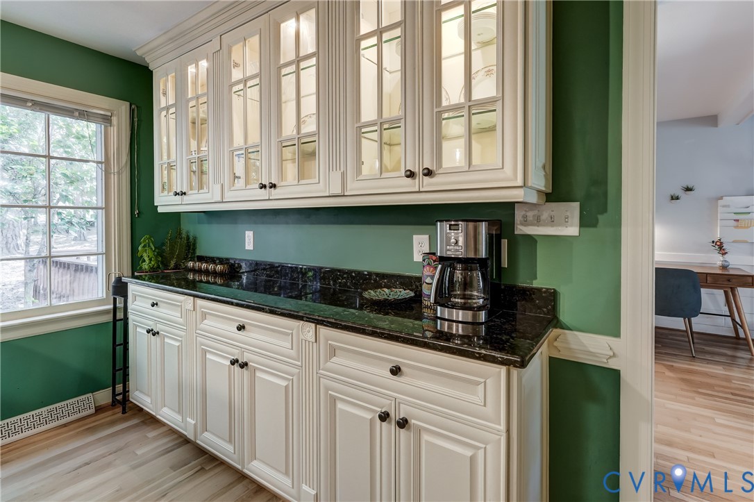 Custom cabinetry with glass-front upper doors, stone countertops, multi-pane window, and wood-finish flooring