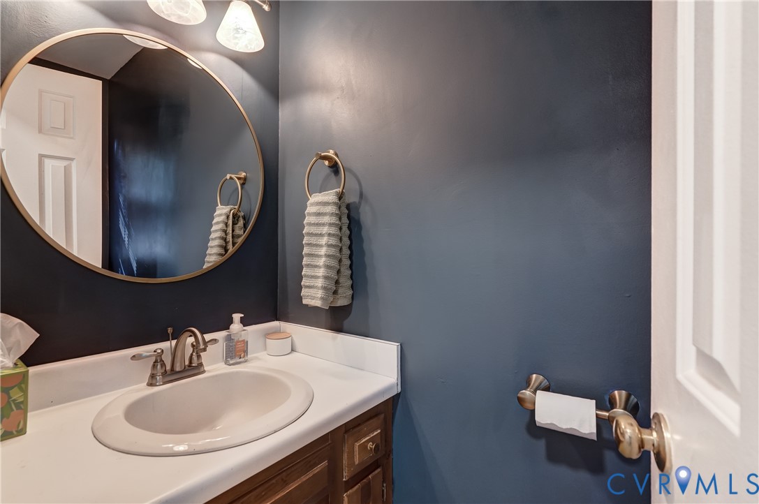 Oval wall mirror with a gold-tone frame, white countertop with an integrated basin, metal hardware, and dual vanity lighting