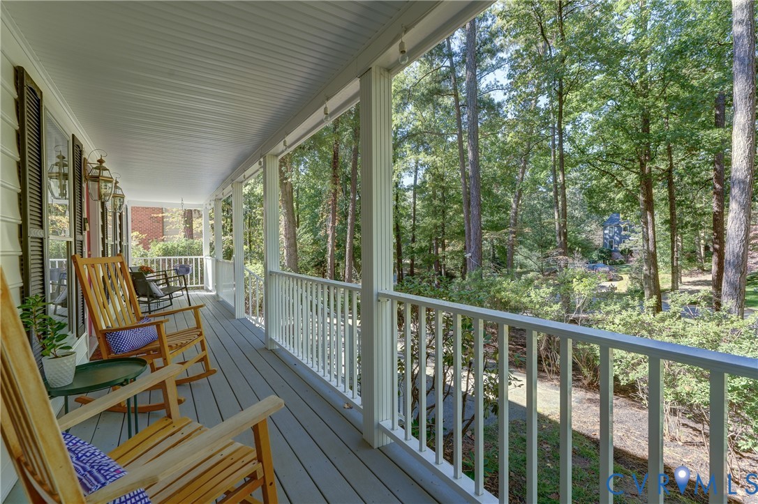 Covered porch featuring wood-finish decking, white baluster railings, beadboard ceiling, and wall-mounted exterior lanterns Covered porch featuring wood-finish decking, white baluster railings, beadboard ceiling, and wall-mounted exterior lanterns