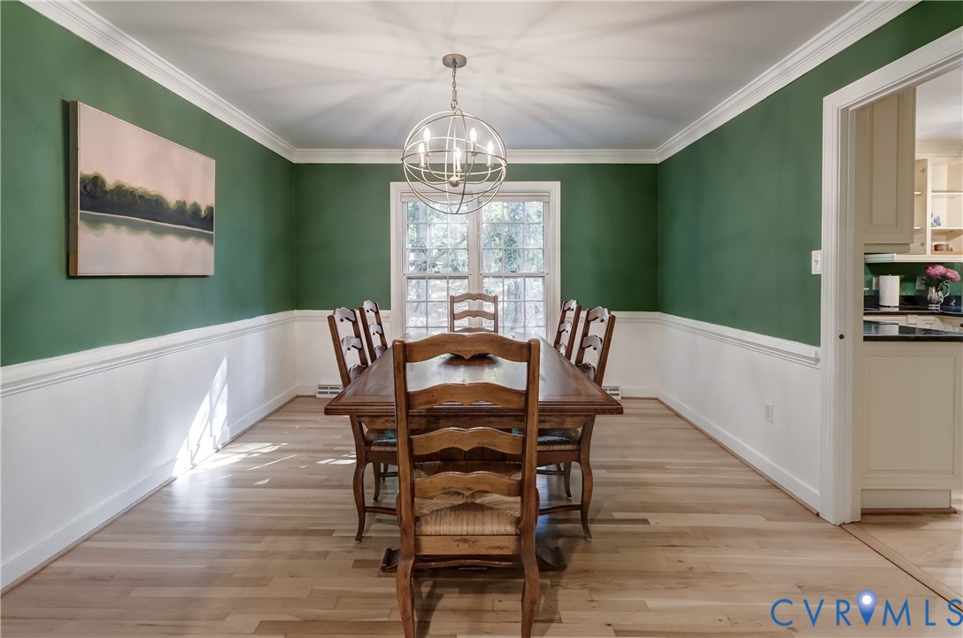 Dining area featuring wood-finish flooring, two-toned wall treatment with chair rail molding, crown molding, and a central spherical pendant chandelier