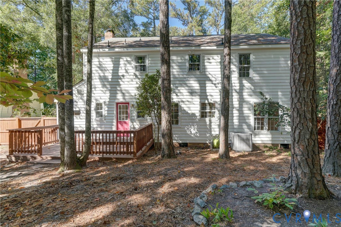 Two-story home exterior featuring light-colored horizontal siding, a wood-finish deck with a rail, and a wooded lot