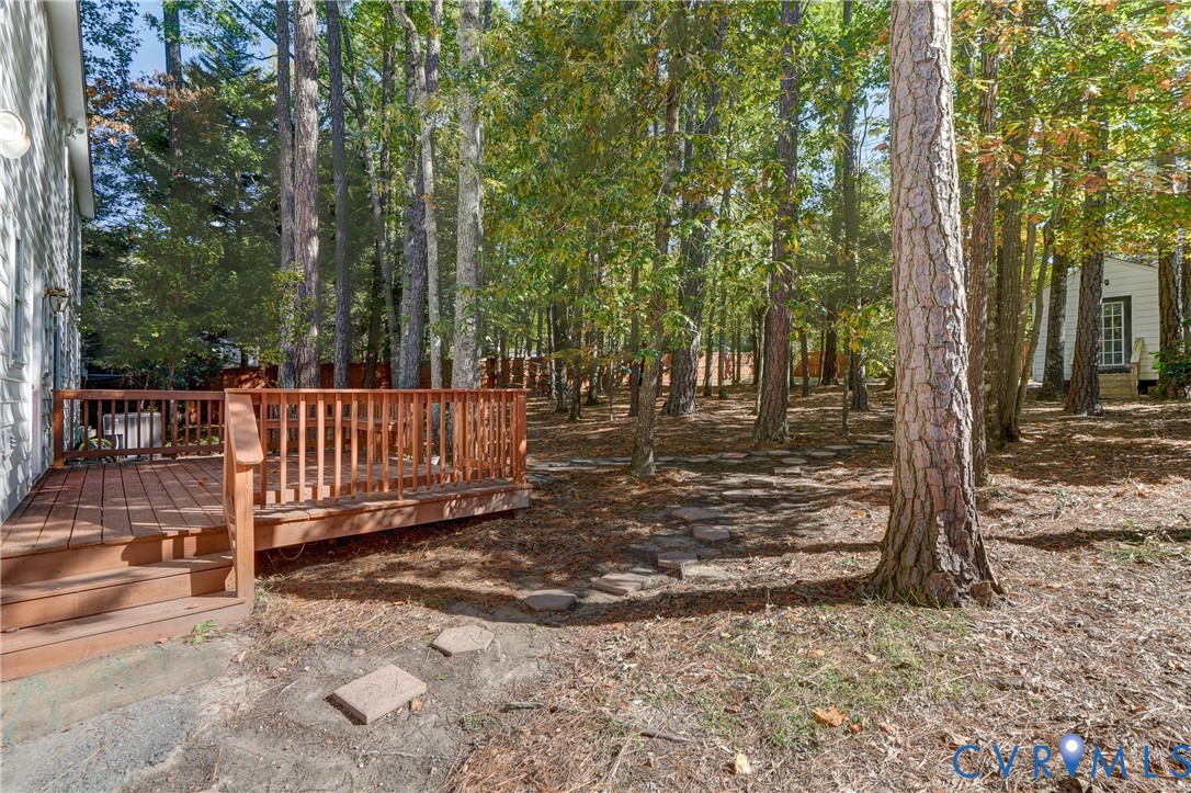 Wood-decking platform with a slatted railing, stone-paver walkway, and mature trees situated on a wooded lot with perimeter fencing