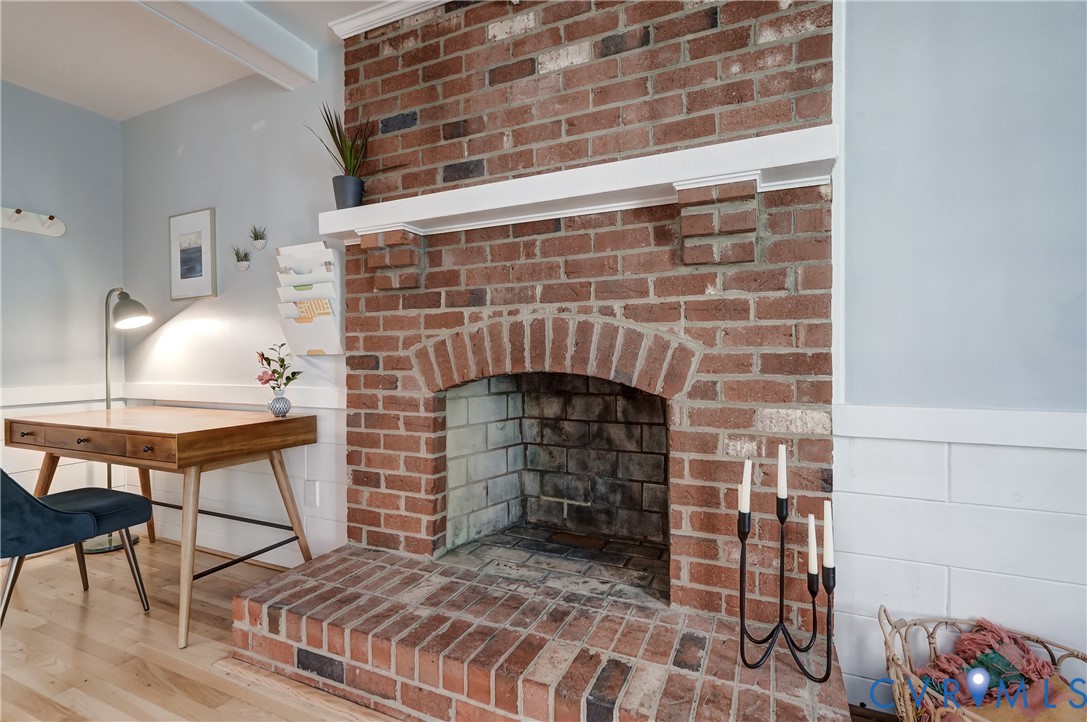 Full-height red brick fireplace featuring a brick hearth and white wooden mantel, complemented by white horizontal wall paneling and wood-finish flooring