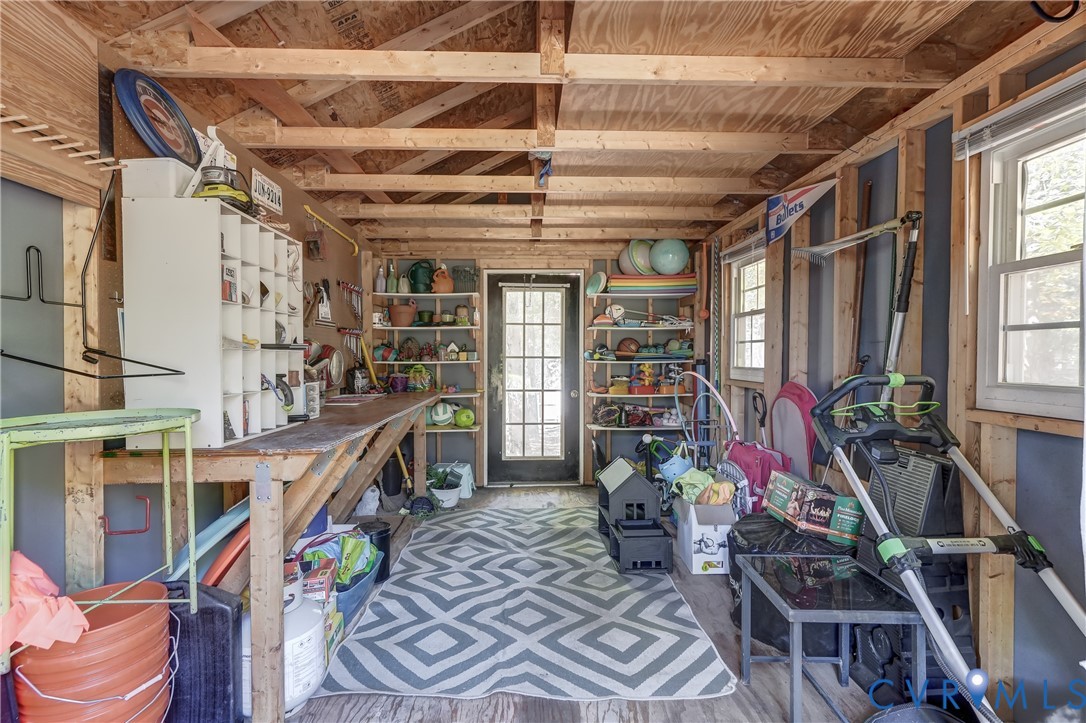 Utility shed with exposed rafter ceiling, built-in wooden workbench, integrated wall shelving, and a glass-paneled exterior door