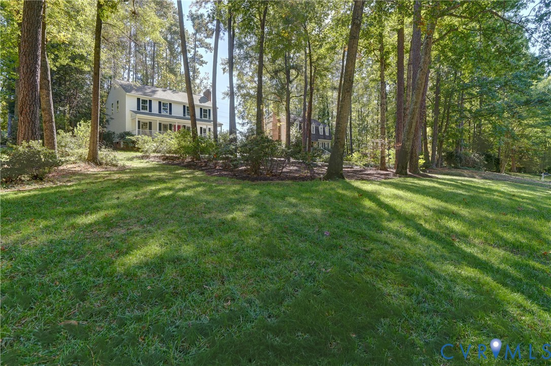 Expansive grass lawn featuring mature trees and established landscaping surrounding a two-story exterior with a covered front porch and multi-pane windows Expansive grass lawn featuring mature trees and established landscaping surrounding a two-story exterior with a covered front porch and multi-pane windows
