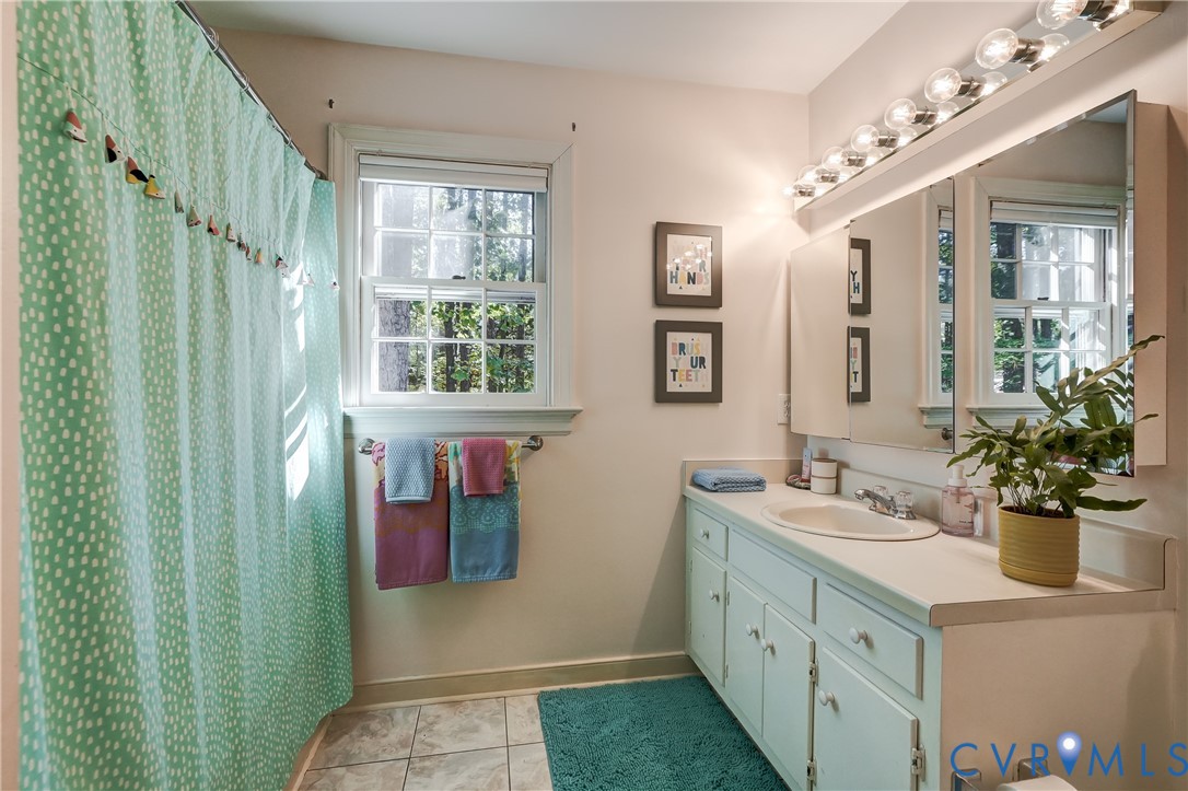 Bathroom featuring a light-toned vanity with an integrated basin, a tri-fold medicine cabinet, a multi-bulb vanity light fixture, and a window with a paneled design