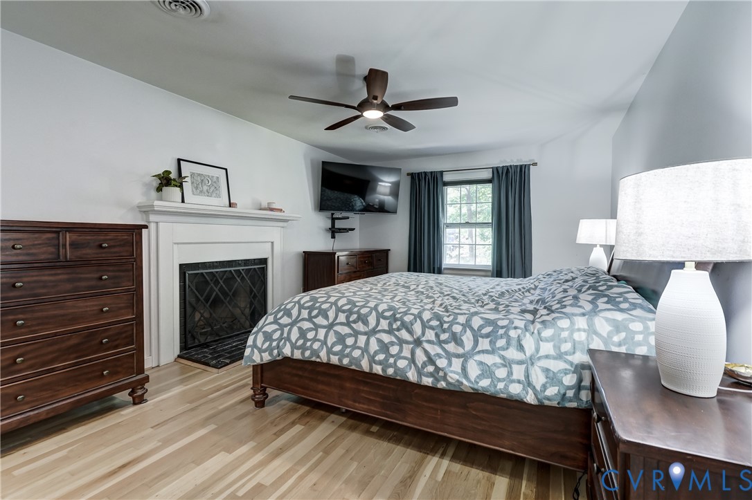 Wood-finish flooring, fireplace with a white mantel, and a ceiling fan