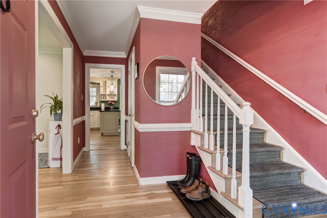 Foyer featuring wood-finish flooring, white crown molding, chair rail trim, and a staircase with white balusters and handrail