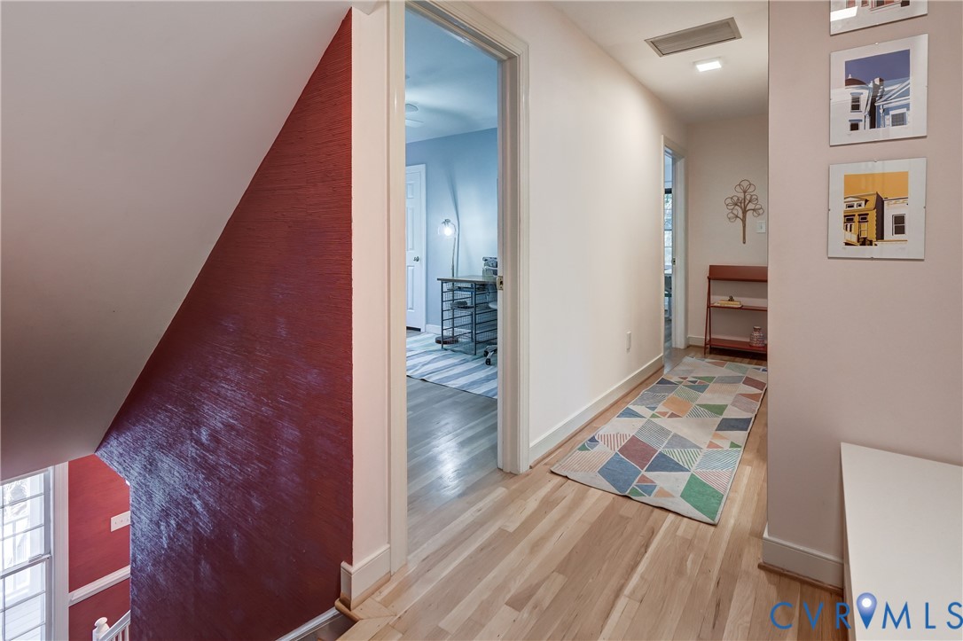 Hallway featuring light-toned wood-finish flooring, recessed ceiling lighting, and a prominent red-painted textured accent wall
