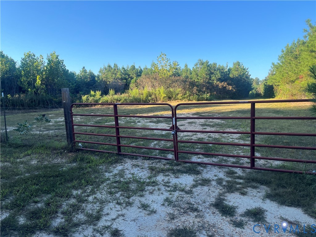 Expansive cleared lot featuring a metal gate, perimeter fencing, and mature tree borders