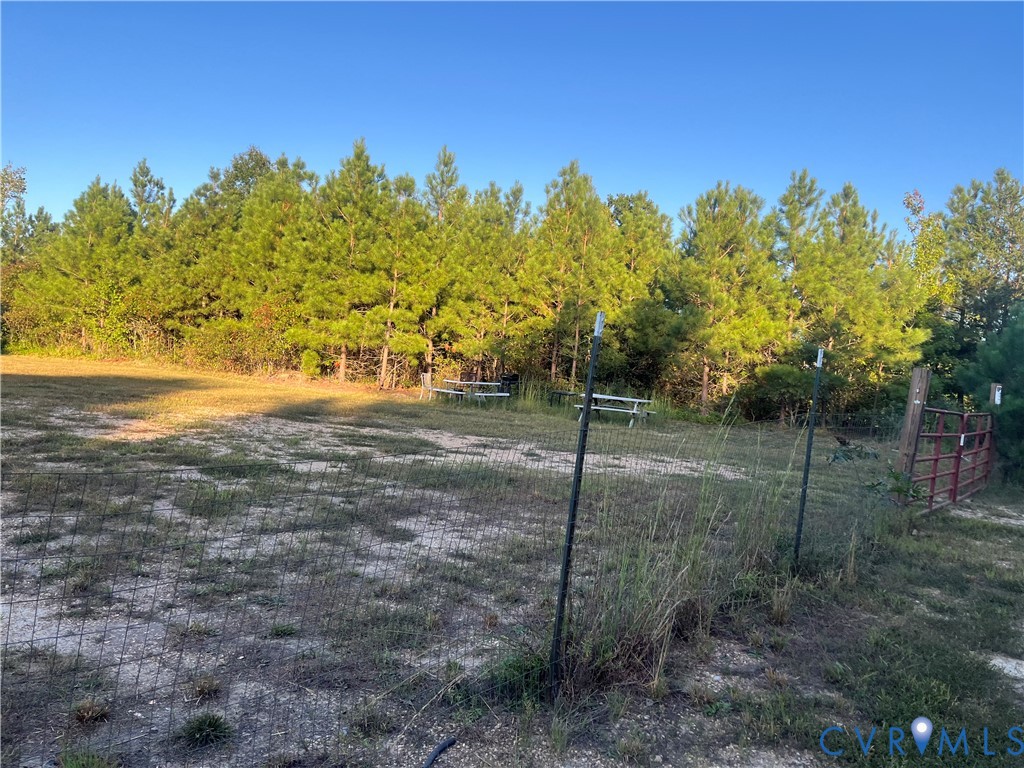Open acreage featuring wire mesh fencing, a metal gate, and a tree-lined perimeter