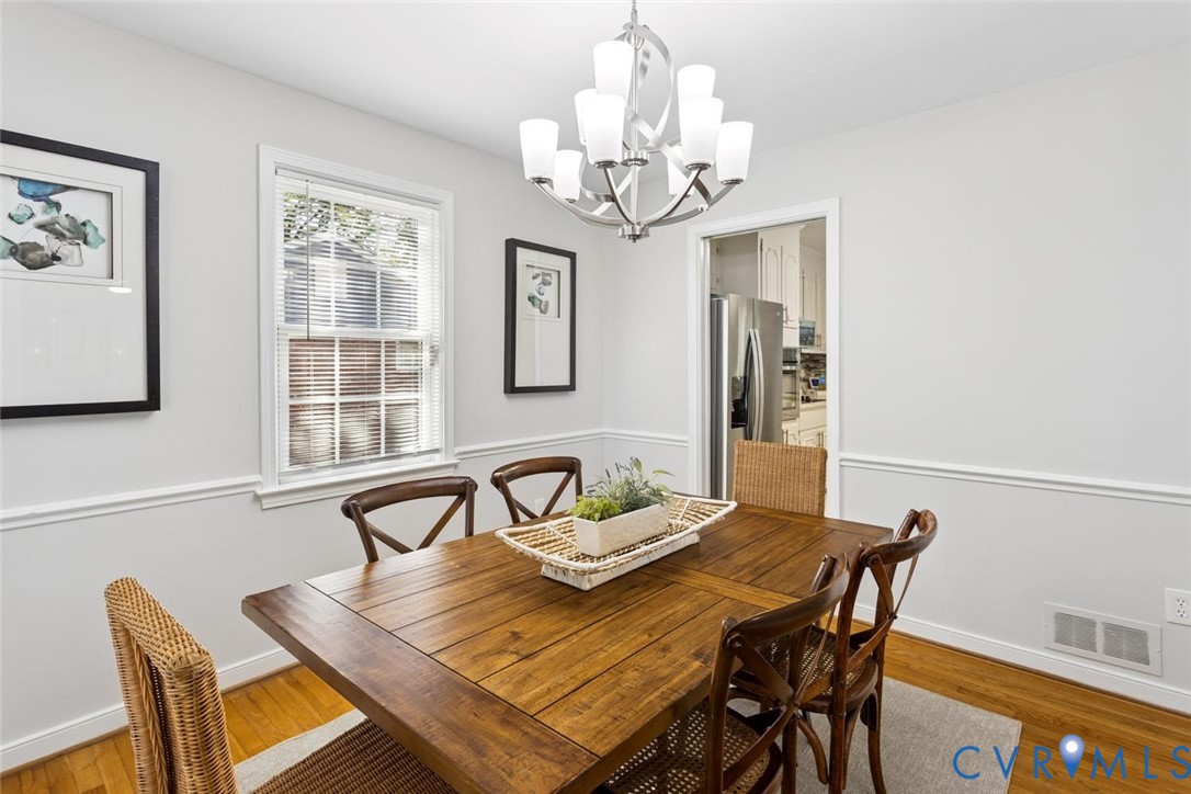 Dining area featuring wood-finish flooring, chair rail molding, a polished metal multi-light chandelier, and a single-hung window