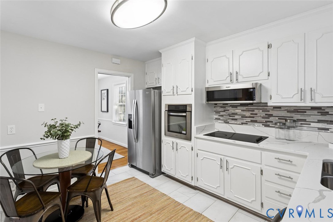Kitchen featuring white cabinetry, quartz countertops, a stone-tile backsplash, and integrated stainless steel appliances including a wall oven, microwave, and refrigerator