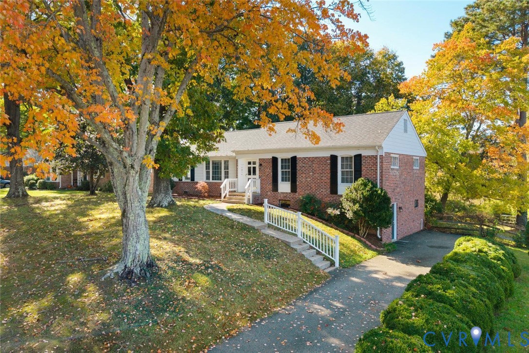 Brick exterior featuring shuttered windows, a gabled roof, white wooden railing, and an asphalt driveway