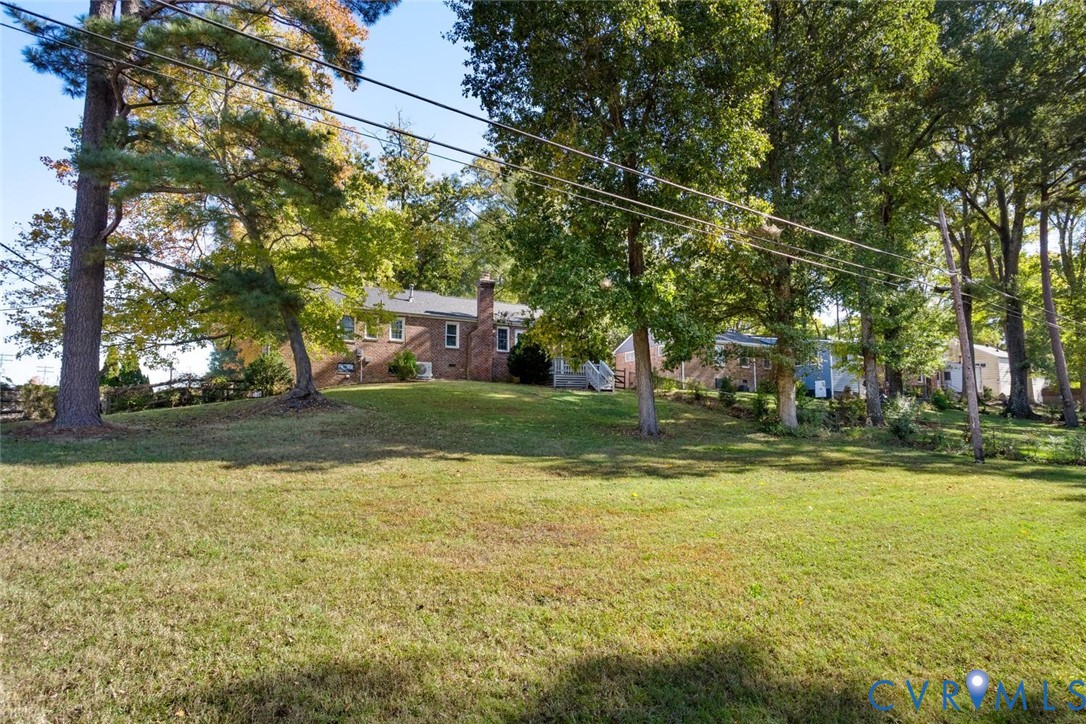 Expansive lawn featuring mature trees and a brick exterior with a prominent chimney