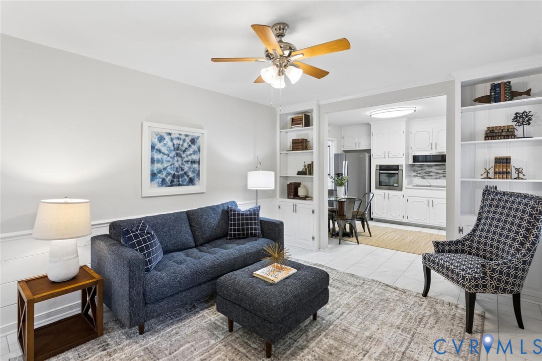 Living area featuring built-in floor-to-ceiling shelving, chair rail molding, and a multi-blade ceiling fan with integrated lighting