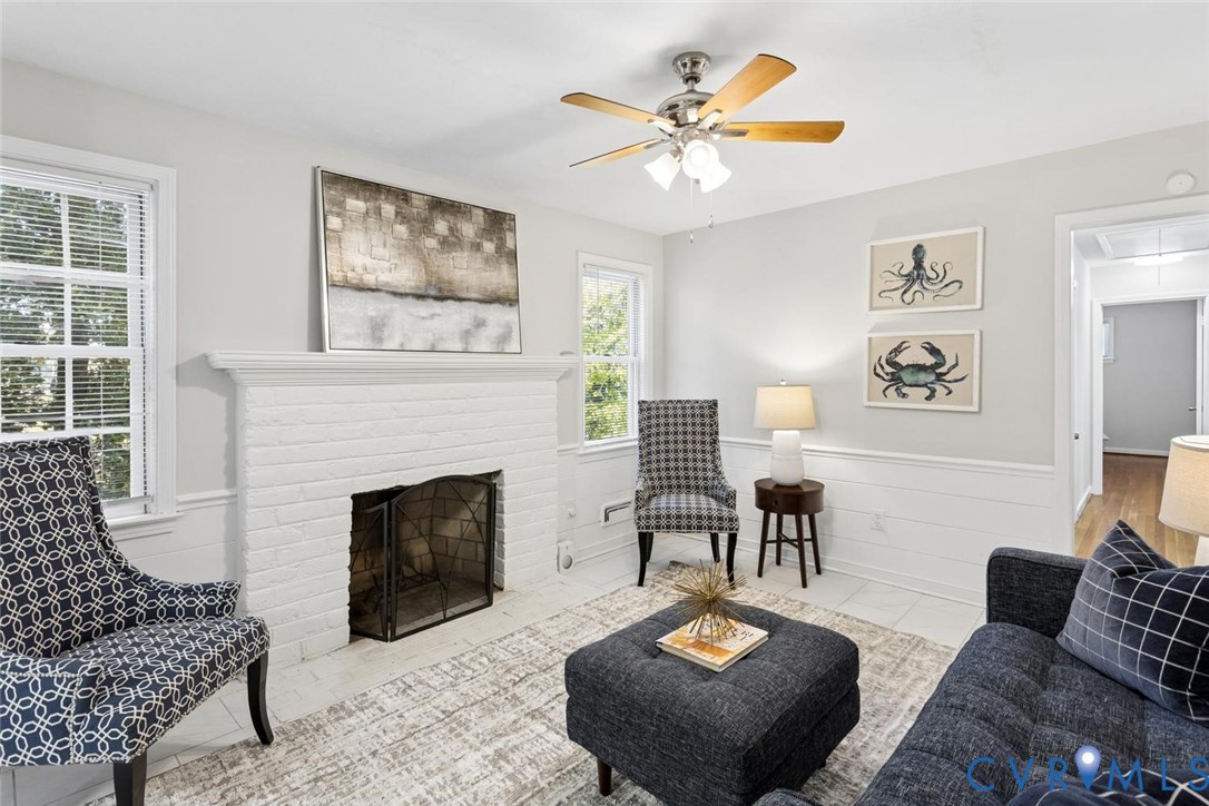Painted brick fireplace with a mantel, chair rail molding, horizontal wall paneling, and a multi-blade ceiling fan