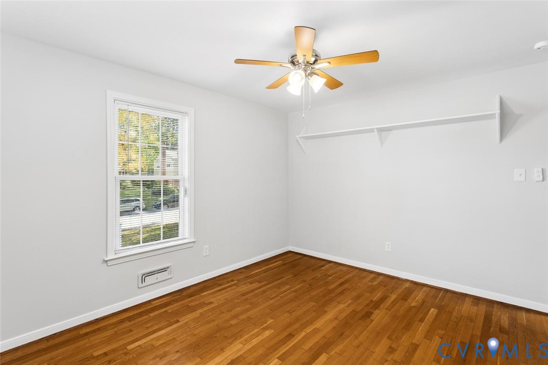 Wood-finish flooring, white walls, double-hung window with muntins, ceiling fan with light kit, and built-in wall shelving