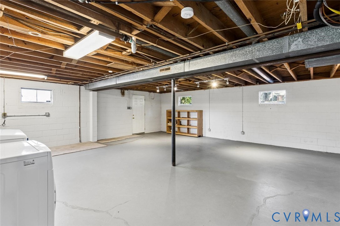 Unfinished lower level featuring painted concrete block walls, painted concrete flooring, exposed wood joist ceilings, and multiple windows