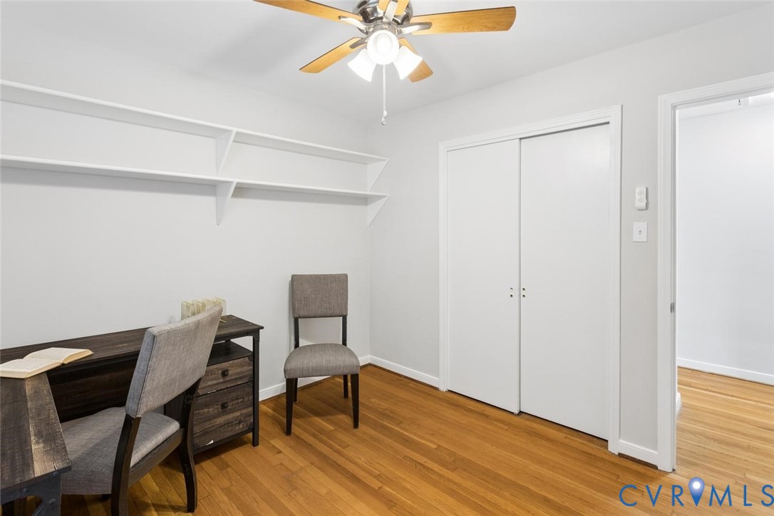 Room featuring wood-finish flooring, built-in wall shelving, a sliding-door closet, and a ceiling fan with integrated lighting