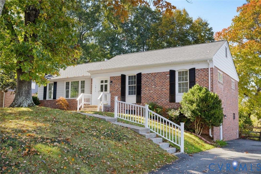 Brick exterior featuring white siding, multi-pane windows with shutters, and a white railed staircase leading to the entrance
