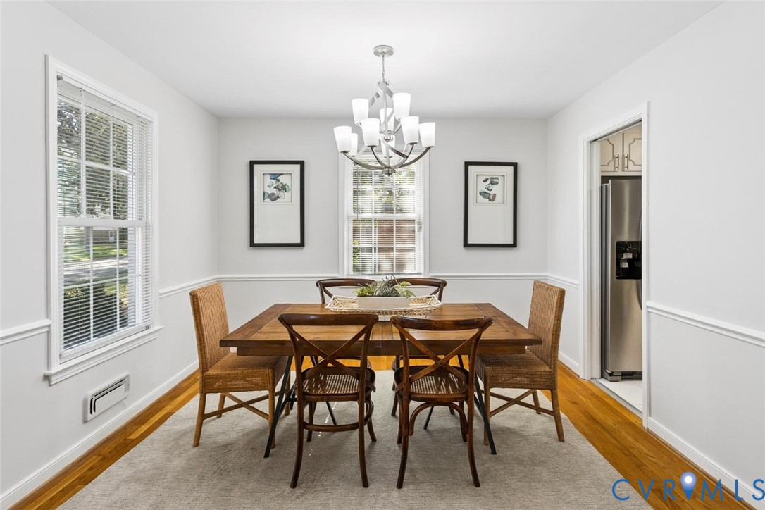 Dining area featuring hardwood flooring, chair rail molding, multi-pane windows, and a tiered chandelier