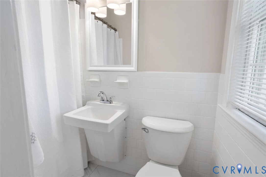 Wall-mounted sink with dual-handle chrome faucet, white subway tile wainscoting, recessed medicine cabinet with integrated lighting, and white porcelain toilet