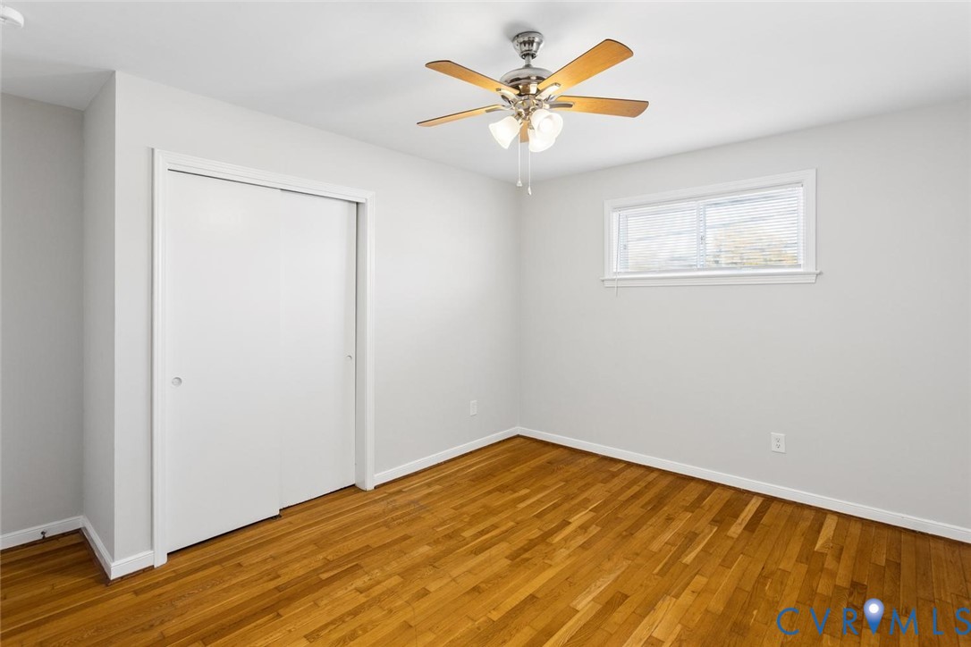 Room featuring wood-finish flooring, a ceiling fan with integrated lighting, and a sliding-door closet
