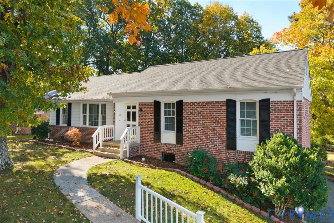 Single-story brick and siding exterior featuring multi-pane windows with shutters, a paved walkway, and a covered entryway with white railing