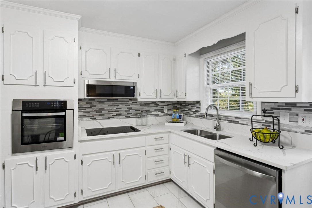 Kitchen featuring white raised-panel cabinetry, stone-finish countertops, stainless steel appliances, multi-toned tiled backsplash, and tile flooring