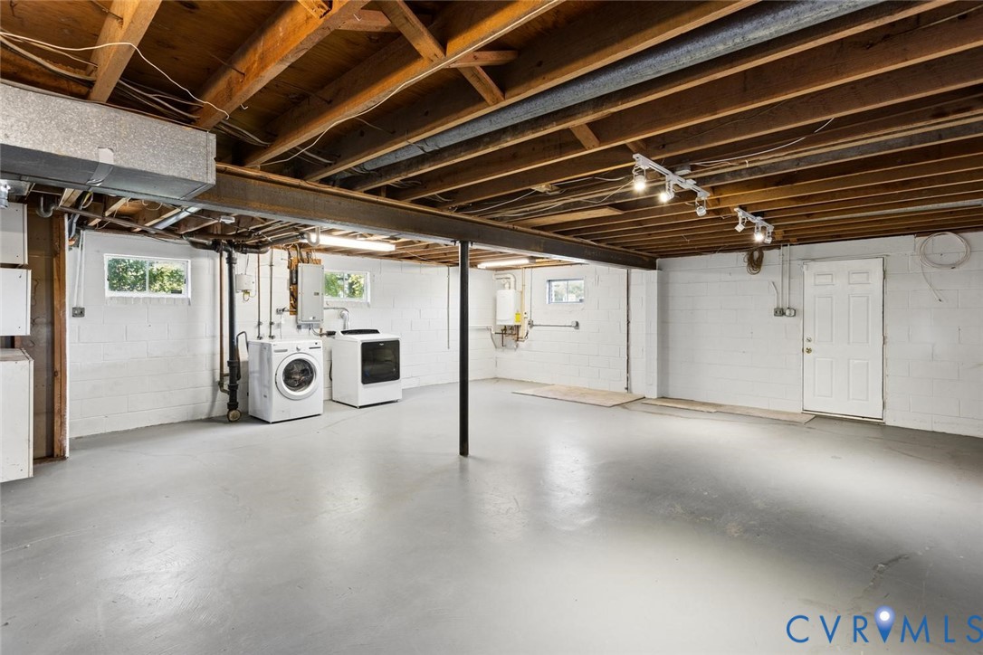 Unfinished lower level featuring exposed wood joist ceilings, painted concrete block walls, painted concrete flooring, built-in laundry hookups, and a dedicated exterior access door