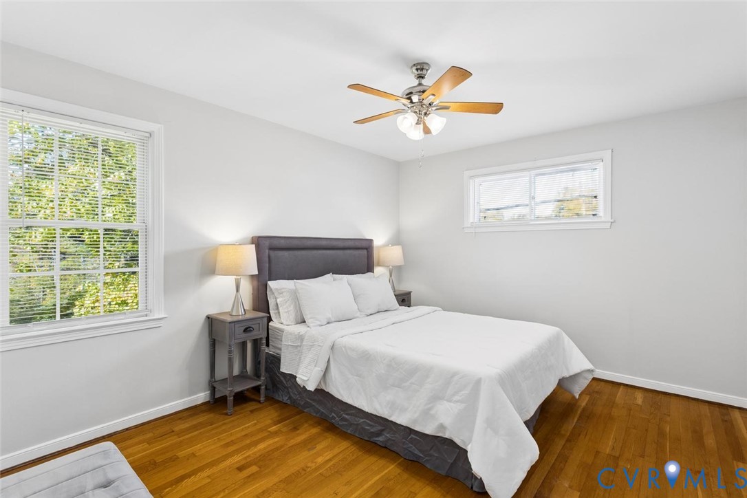 Bedroom interior featuring wood-finish flooring, neutral wall paint, two double-hung windows, and a brushed metal ceiling fan with integrated light fixture