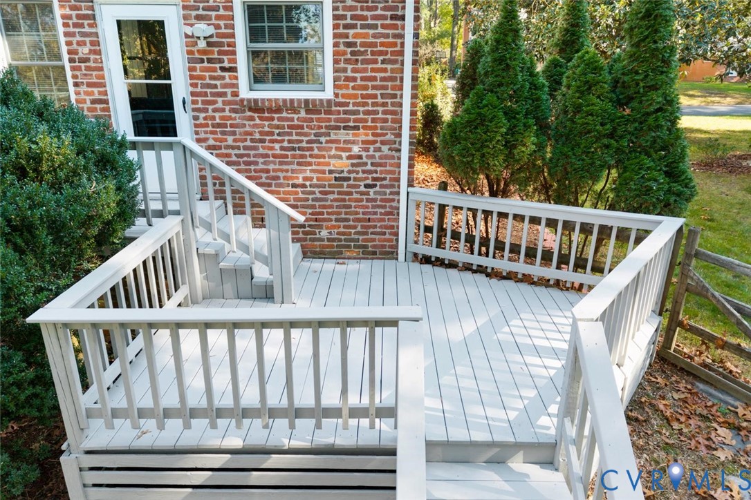 Multi-level painted wood deck featuring custom railings and stairs, set against a red brick exterior with mature landscaping