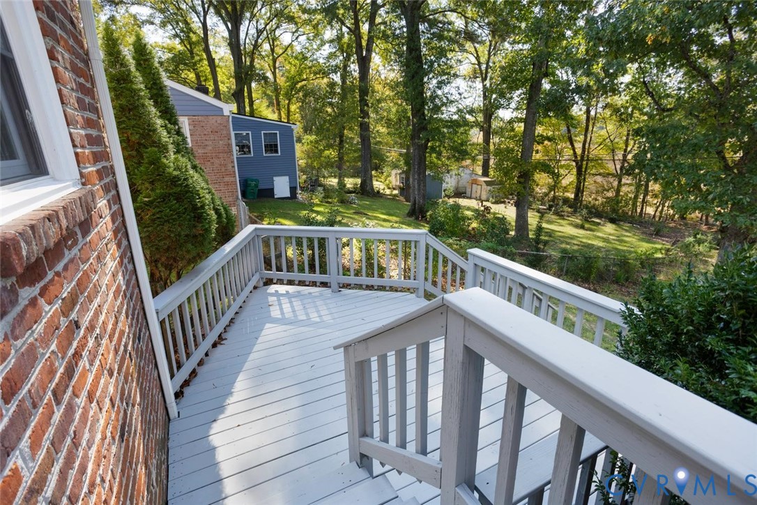 Painted wooden deck with matching railing, brick exterior wall, and tiered wooden stairs overlooking a wooded backyard