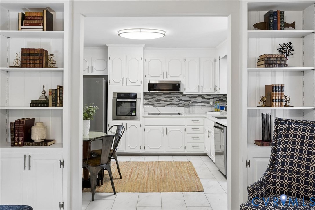Kitchen featuring white raised-panel cabinetry, stainless steel wall oven, mosaic tile backsplash, built-in floor-to-ceiling shelving, and tile flooring