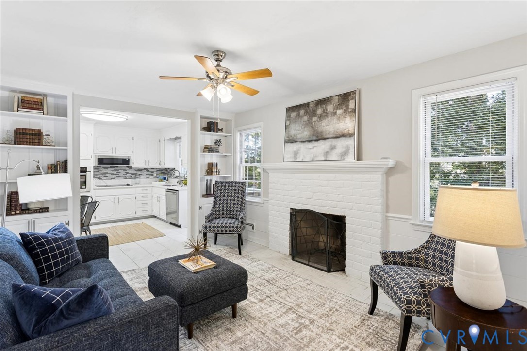 Living area featuring a white brick fireplace with a custom mantle, built-in floor-to-ceiling shelving, and a ceiling fan